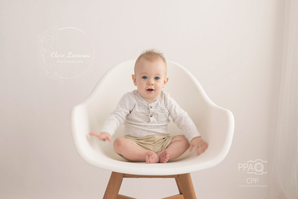 One year old boy sitting on a white chair at a photography session