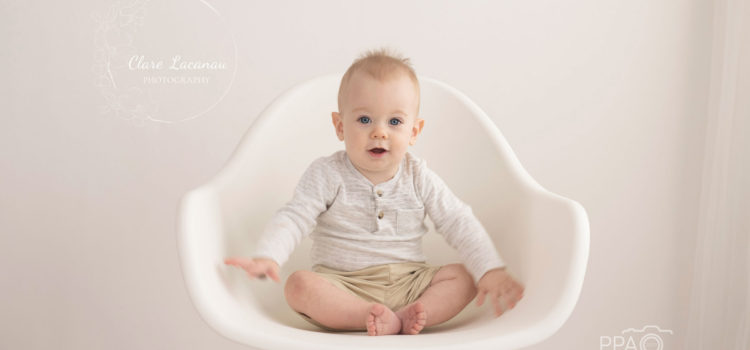One year old boy sitting on a white chair at a photography session